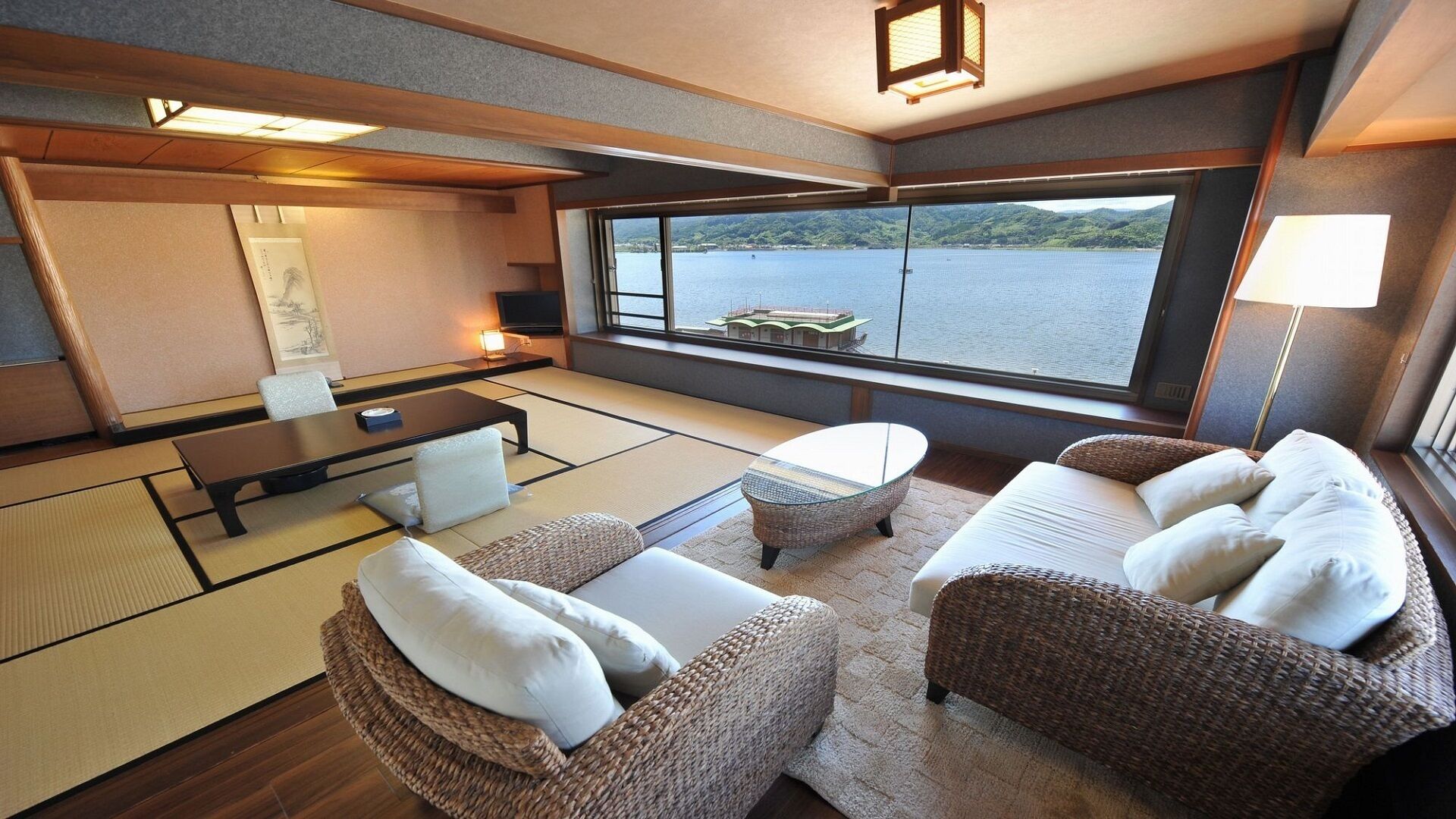 A room with tatami flooring, a low table, a sofa, and a view of a lake.