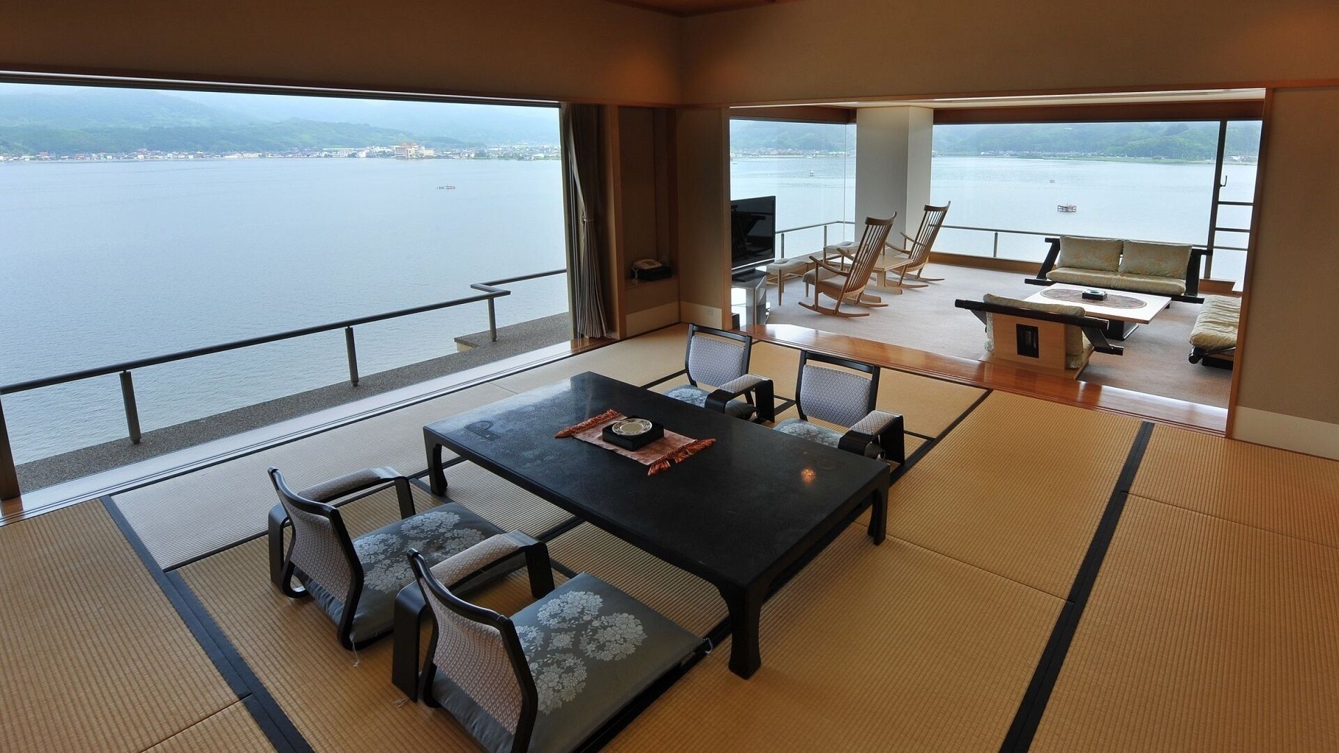 A room with tatami flooring, a dining table with chairs, and a view of a body of water.