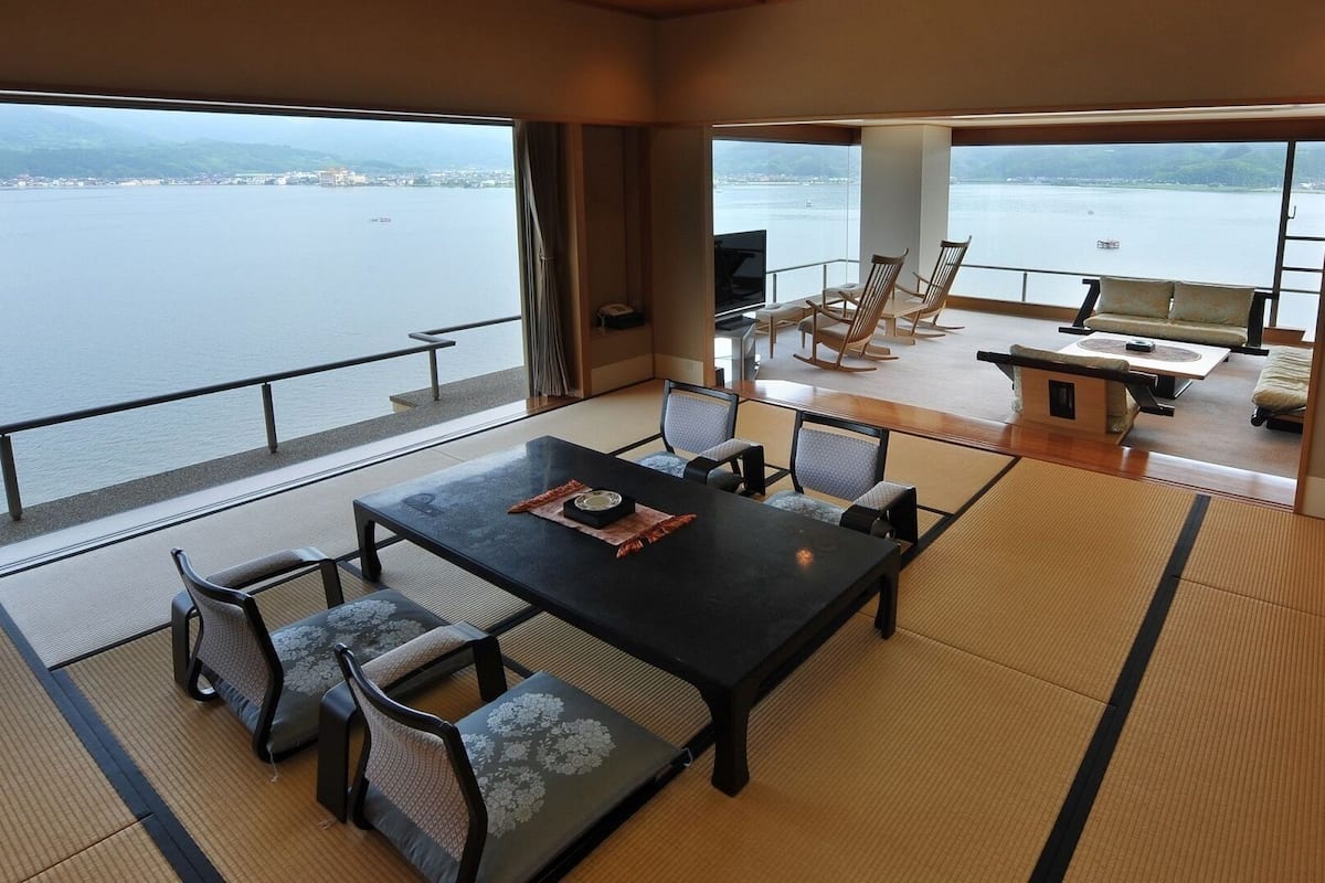 A room with tatami flooring, a dining table with chairs, and a view of a body of water.