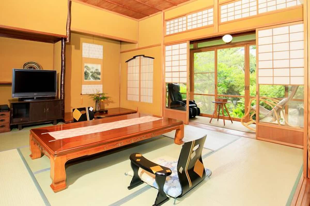 Una habitación con tatamis, una mesa de tatami, un televisor y puertas correderas que dan a un balcón.