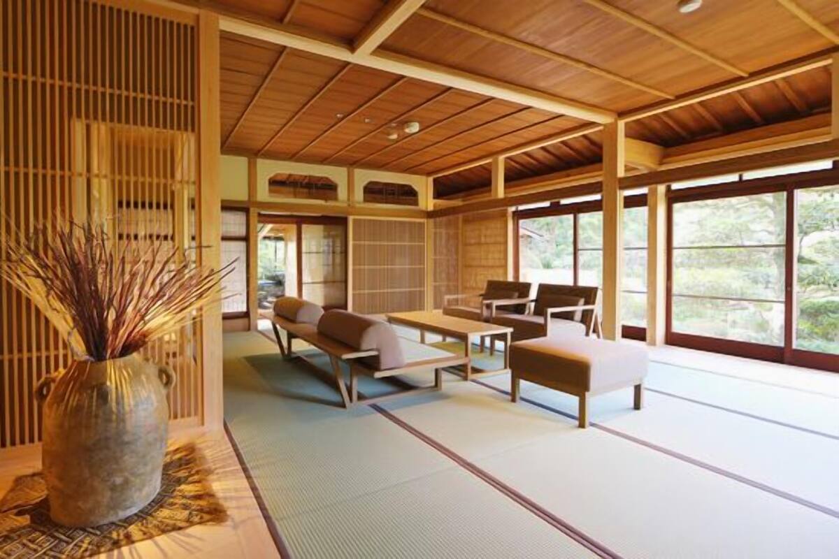 Un interior japonés tradicional con suelo de tatami, techo de madera bajo y un ventanal con vistas al exterior.