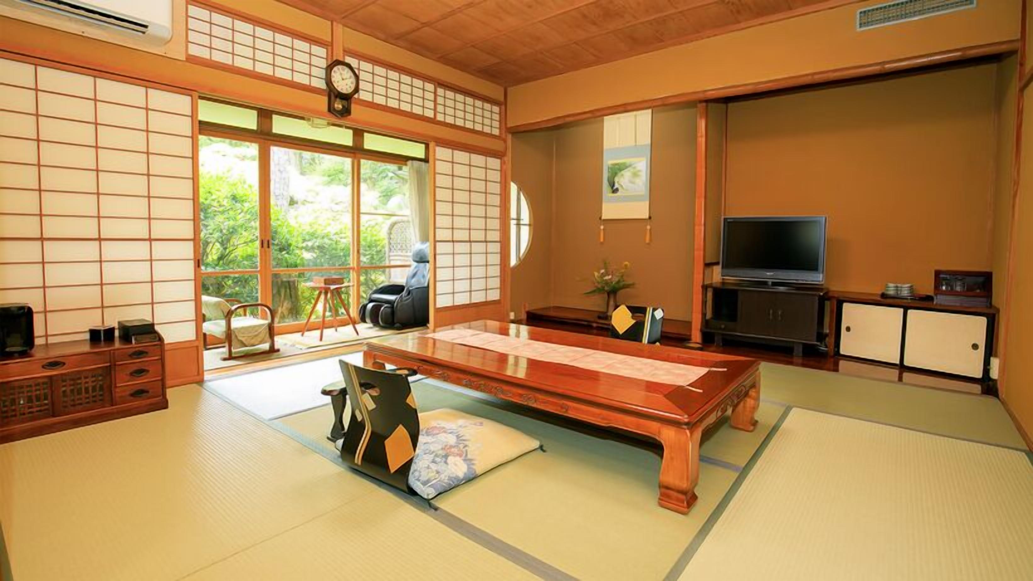 A traditional Japanese-style room with tatami flooring, a low table, a television, and sliding doors.