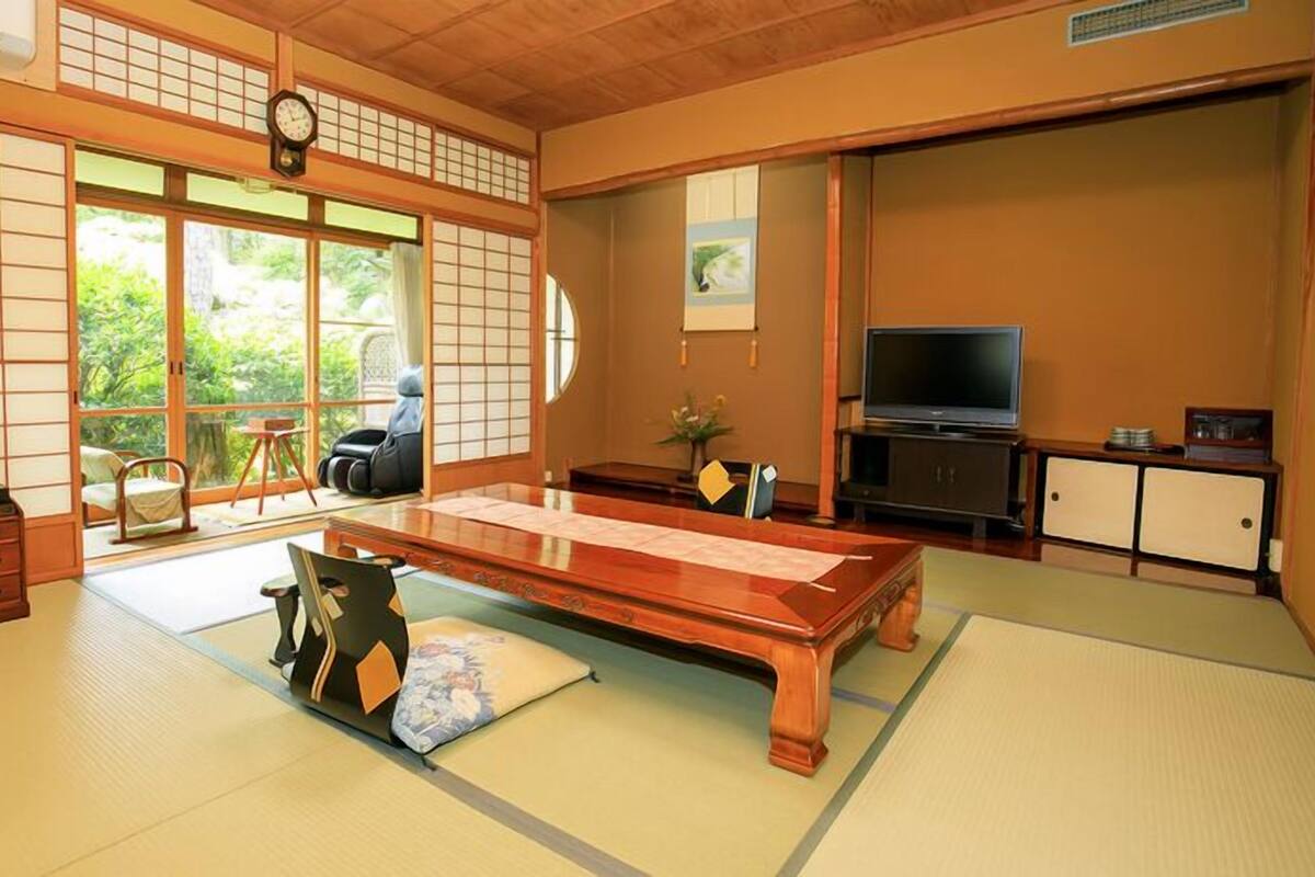 Una habitación tradicional japonesa con suelo de tatami, una mesa baja, un televisor y puertas correderas.