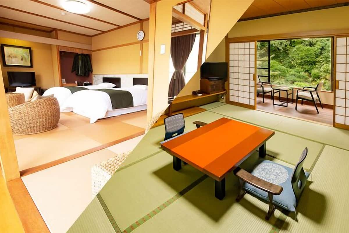 Una habitación tradicional japonesa con suelo de tatami, un futón, una mesa de tatami con cojín y un puertas correderas que dan a un jardín.