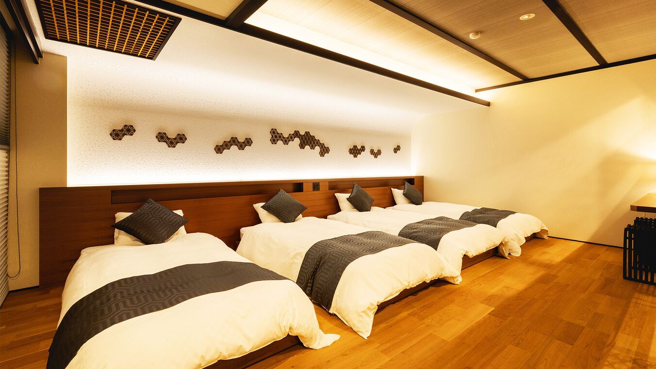 A hotel room with three beds, a wooden headboard, a wall-mounted light fixture, and a ceiling vent.