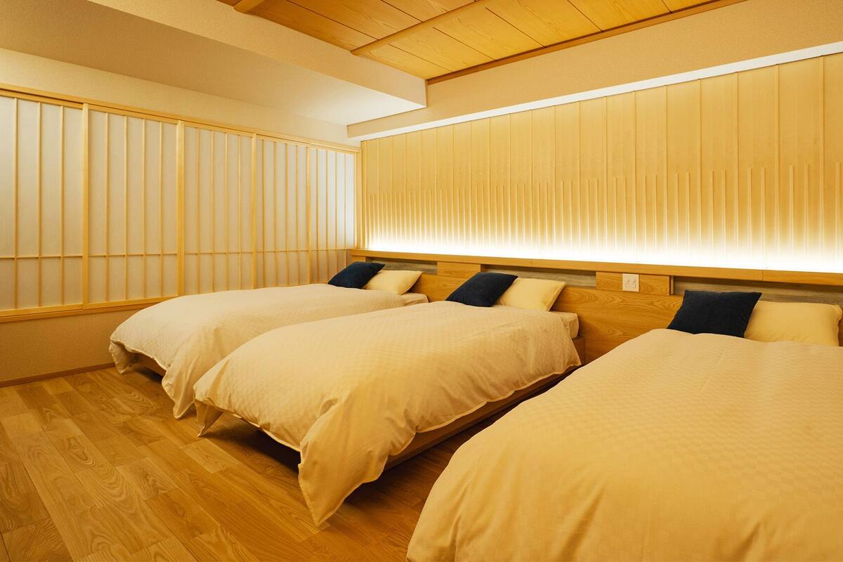 A hotel room with two beds, wooden flooring, and a large window with blinds.