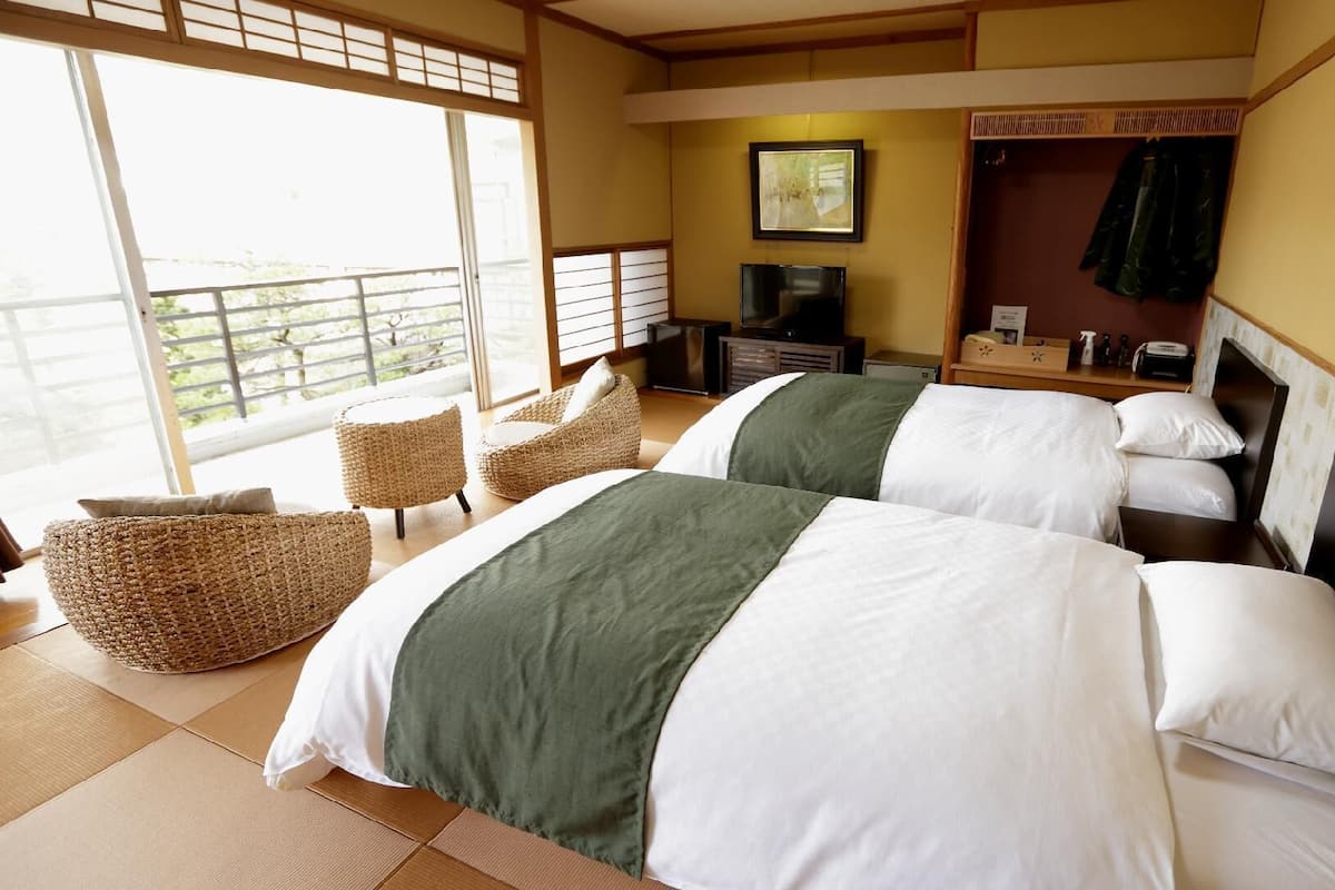 A hotel room with two beds, a TV, a balcony with a view, and a small seating area.