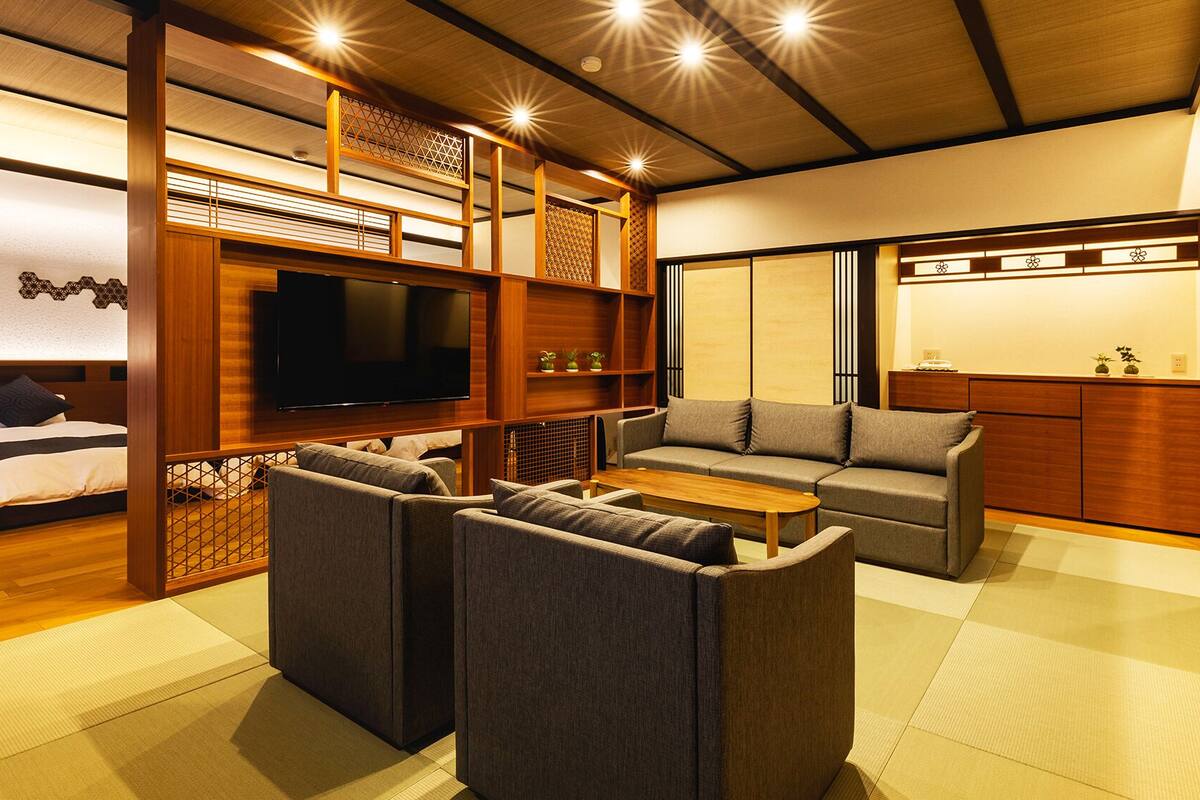 A traditional Japanese-style room with tatami flooring, a low wooden bed, a television, a sofa, and a small table.