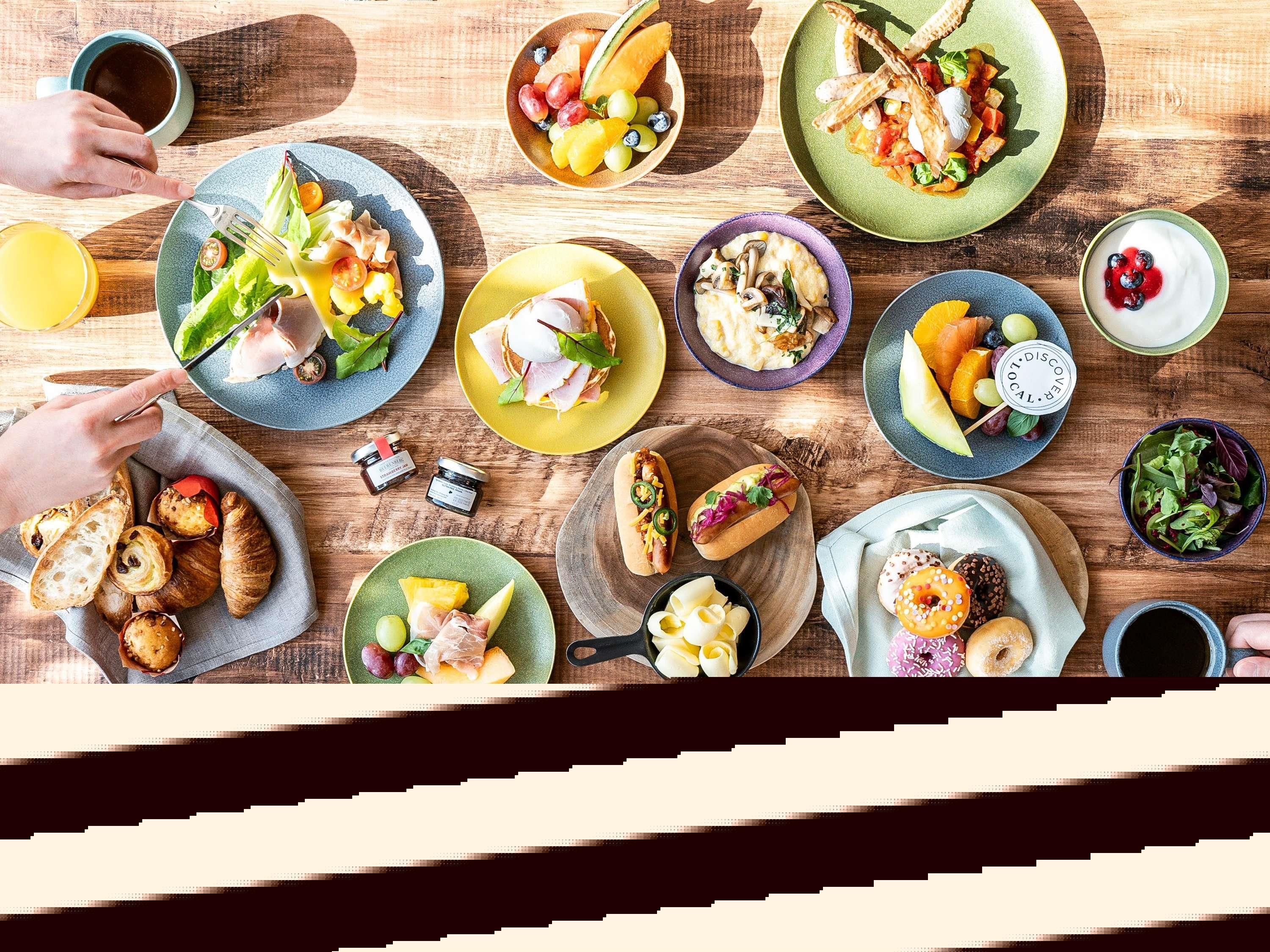 Variedad de alimentos sobre una mesa de madera, como sándwiches, frutas y pasteles.