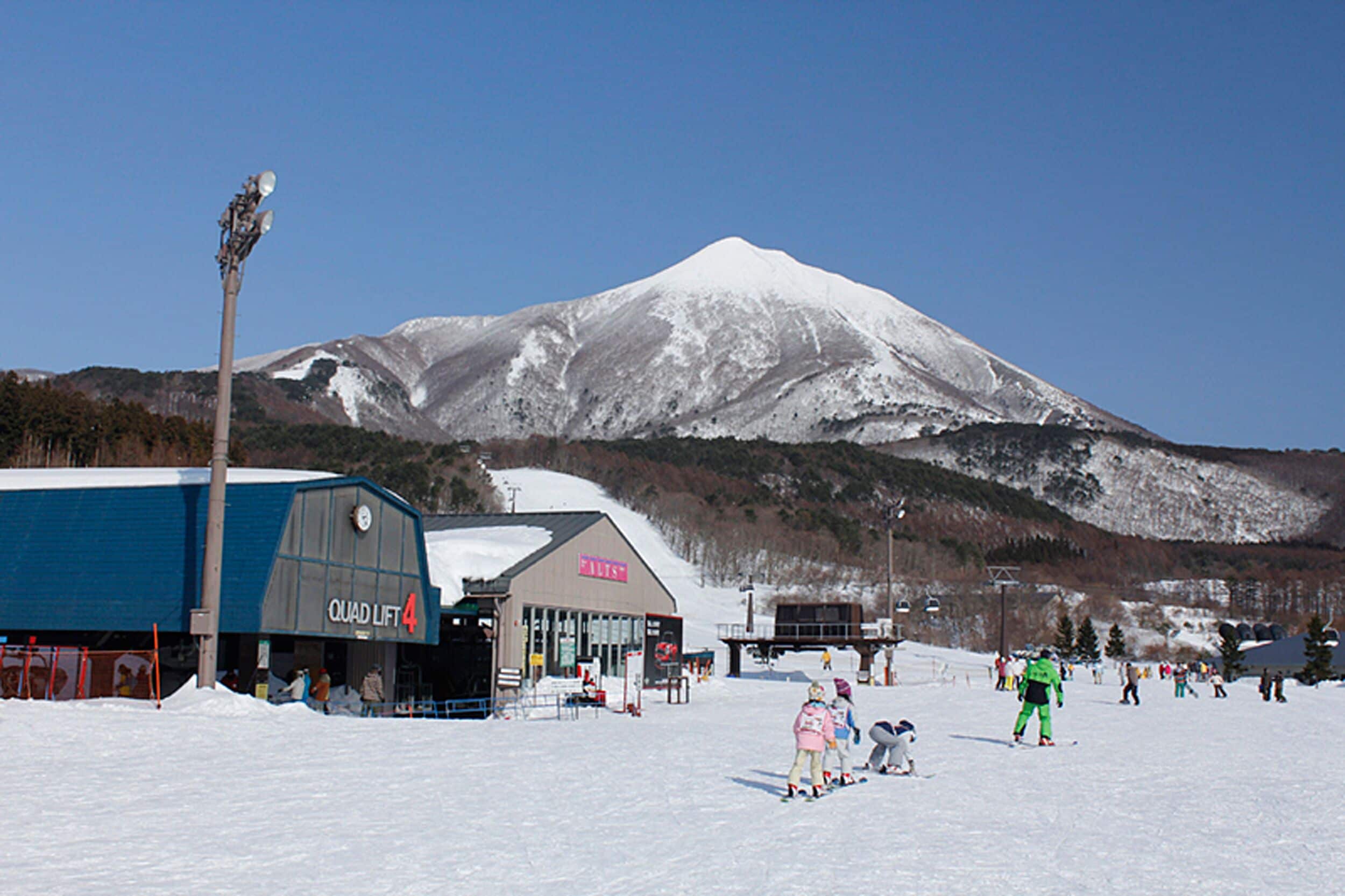 A ski resort with a snow-covered mountain in the background, a building labeled "QUAD LIFT 4", and skiers on the slopes.