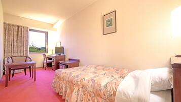 A hotel room with a bed, a desk with a computer, a chair, and a window with curtains.