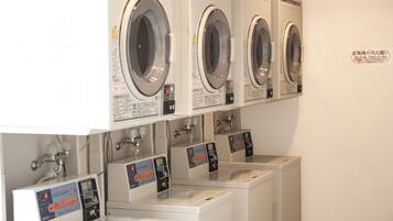 A row of front-loading washing machines with control panels, arranged in a row against a wall.