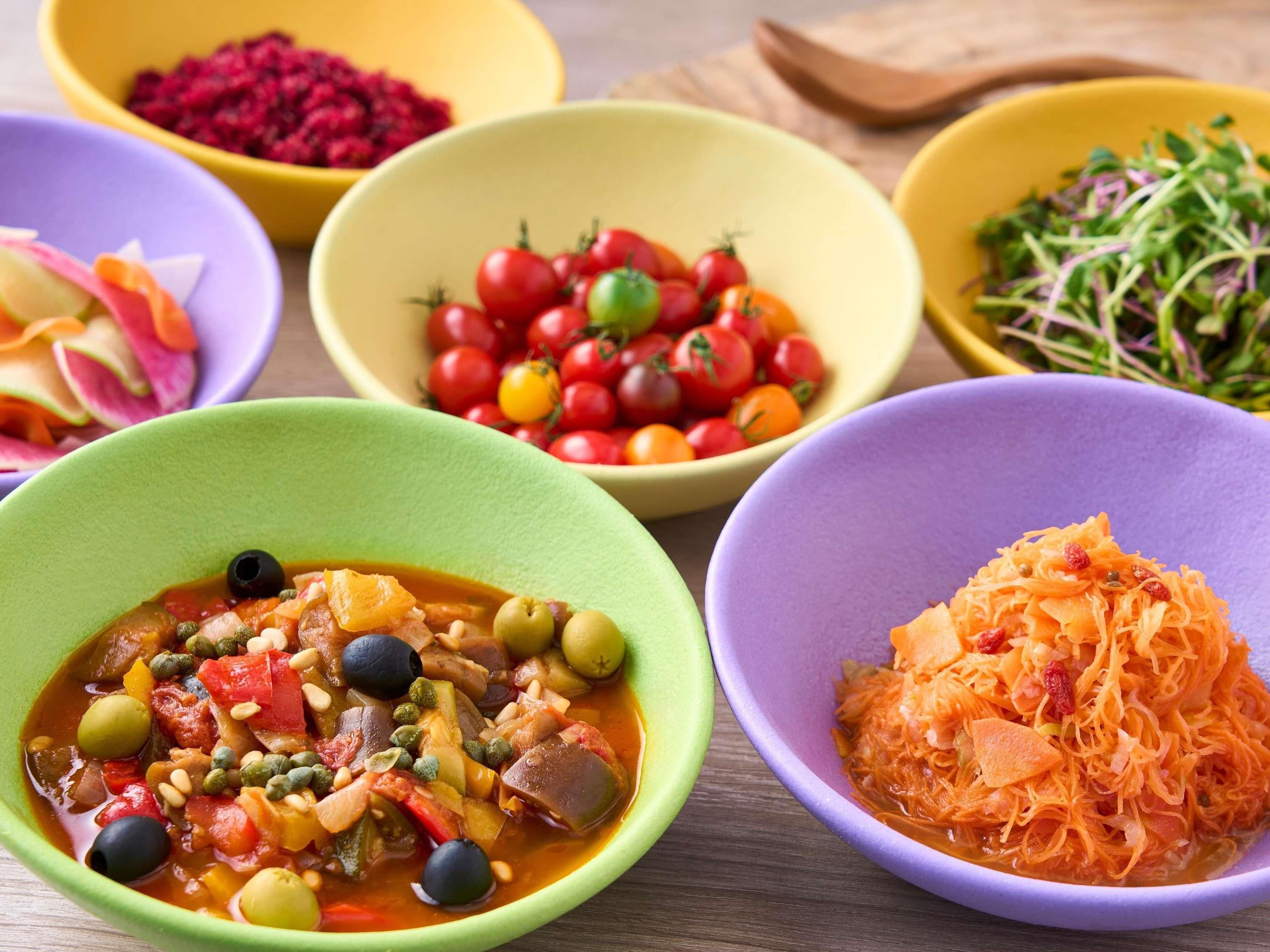 On peut voir une variété de plats colorés servis dans des bols, notamment un ragoût de légumes, des tomates cerises et des carottes râpées.