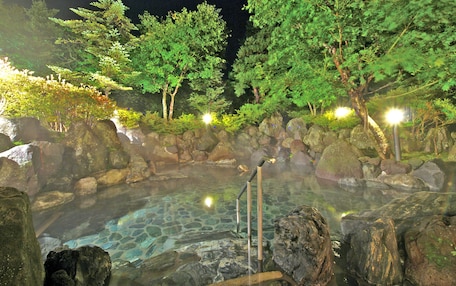 A hot spring area with a stone pool surrounded by rocks and trees, illuminated by lights.