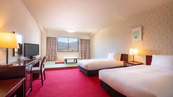 A hotel room with two beds, a desk with a TV, a window with a mountain view, and a red carpet.