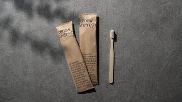 Two brown paper bags labeled "renew & refresh" and a wooden toothbrush on a textured gray surface.