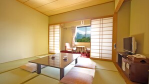 Et traditionelt japansk rum med tatami-gulv, et lavt bord med puder, skydeluger i shoji-stil og et fjernsyn.