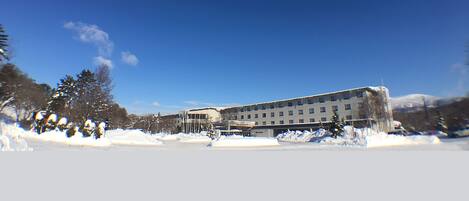 Un edificio grande de varios pisos con techo plano, rodeado de nieve en el suelo y árboles.