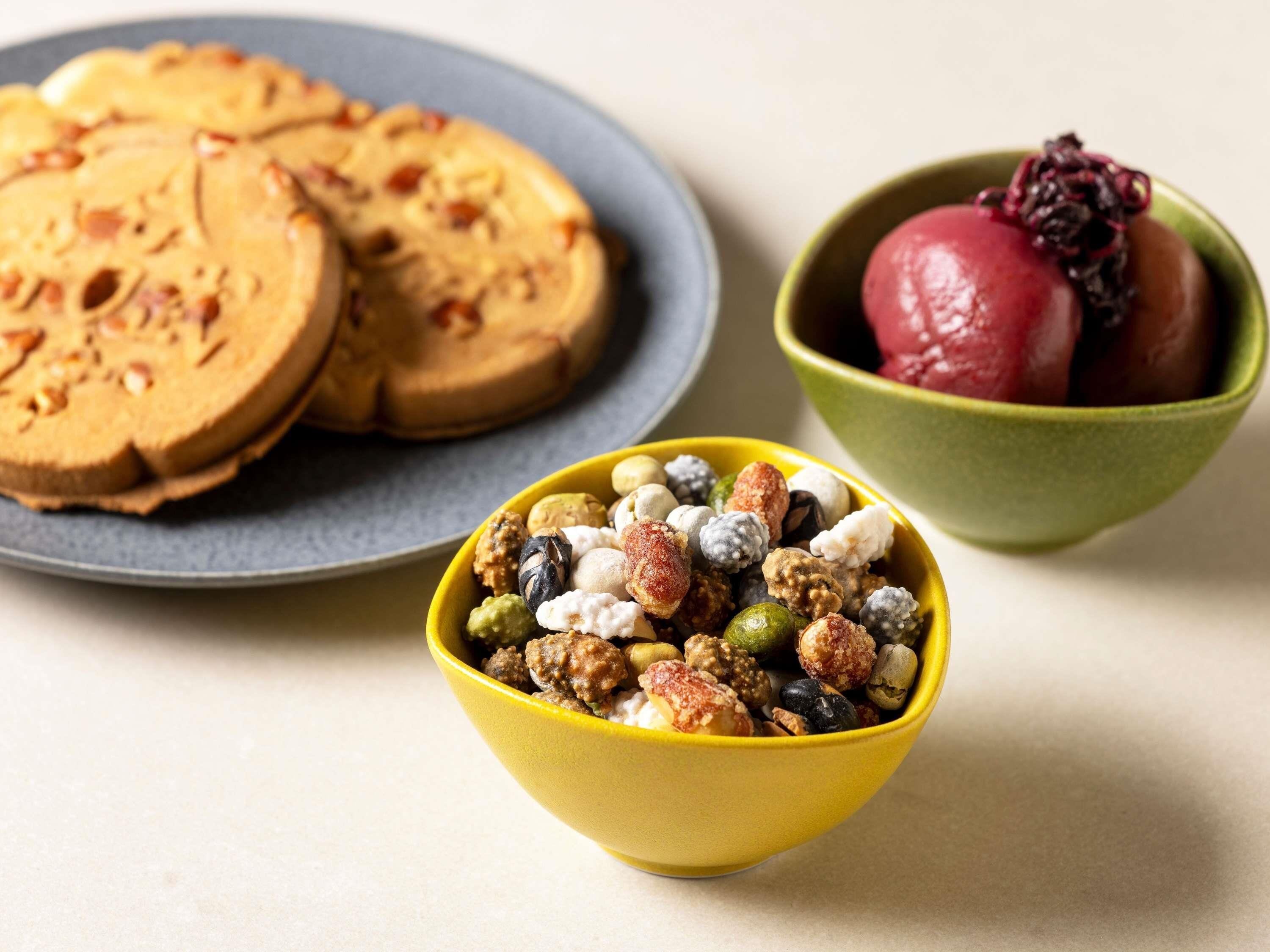 A plate of sliced cookies, a bowl of mixed nuts, and a bowl with a red fruit.