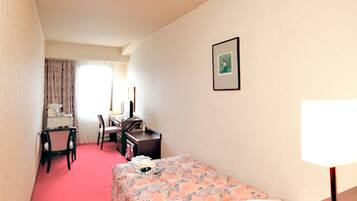 A hotel room with a single bed, a desk with a chair, a lamp, and a framed picture on the wall.