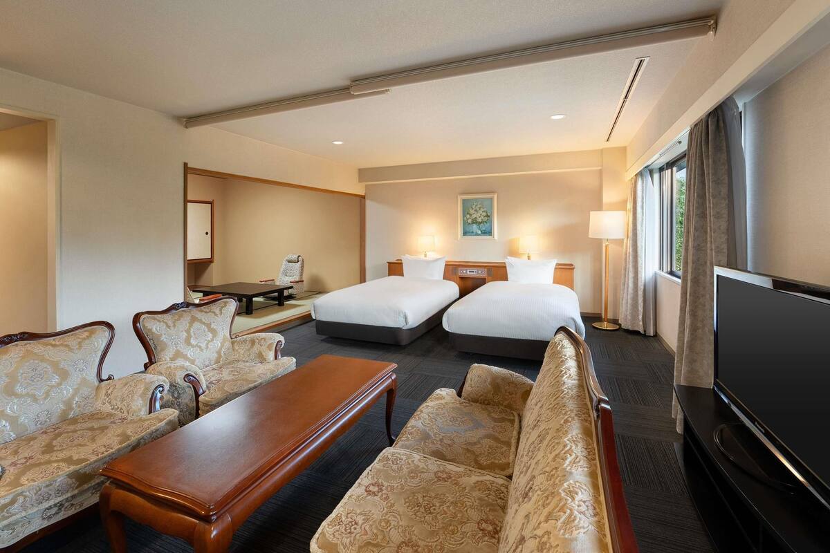A hotel room with two beds, a sofa, a coffee table, a TV, and a desk with a computer.
