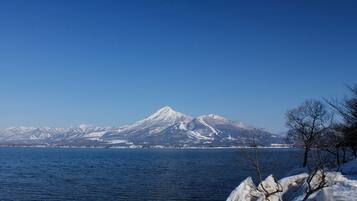 A snow-covered mountain range with a clear blue sky and calm water in the foreground.
