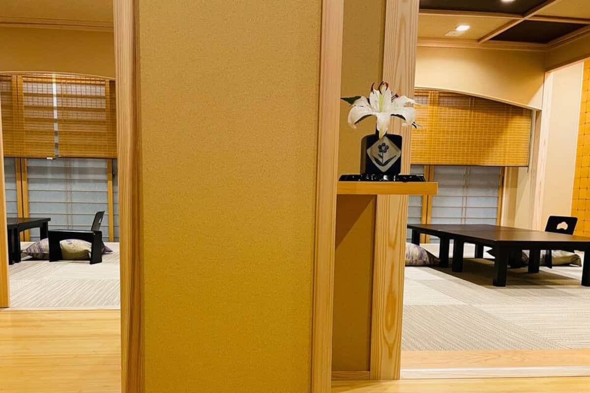 A room with a wooden floor, a table, chairs, a decorative vase, and a window with blinds.