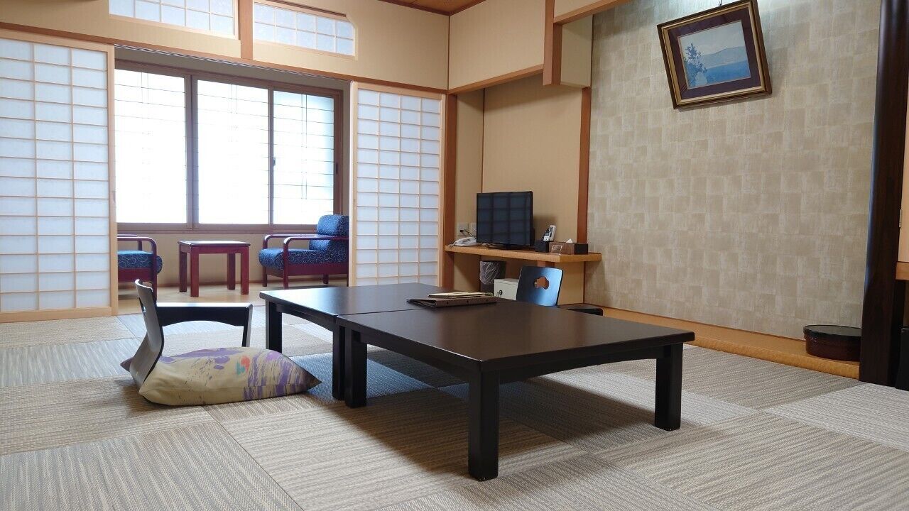 Una habitación japonesa tradicional con suelo de tatami, una mesa baja, sillas, un televisor y un cuadro en la pared.