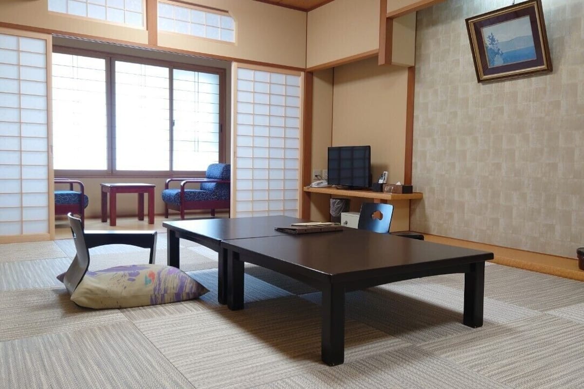 A traditional Japanese room with tatami flooring, a low table, chairs, a TV, and a picture on the wall.