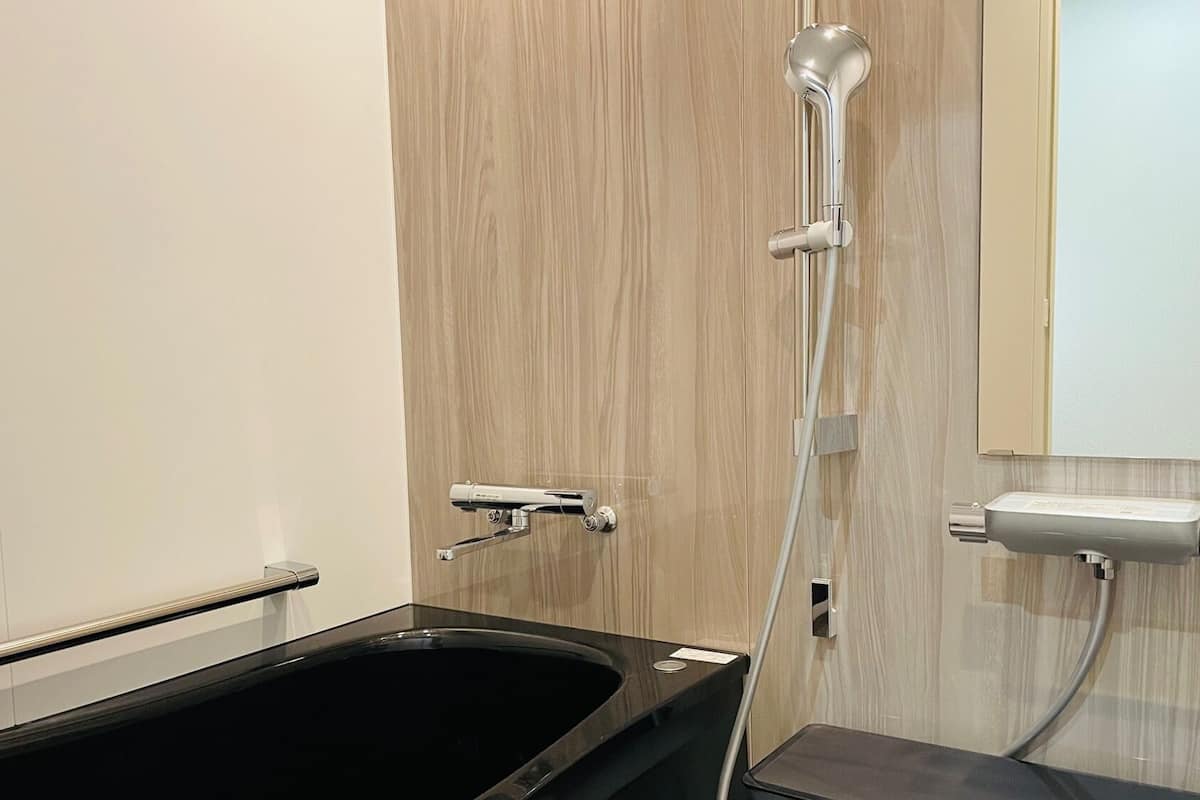 A modern bathroom with a black bathtub, a wooden vanity, and a shower with a handheld showerhead.