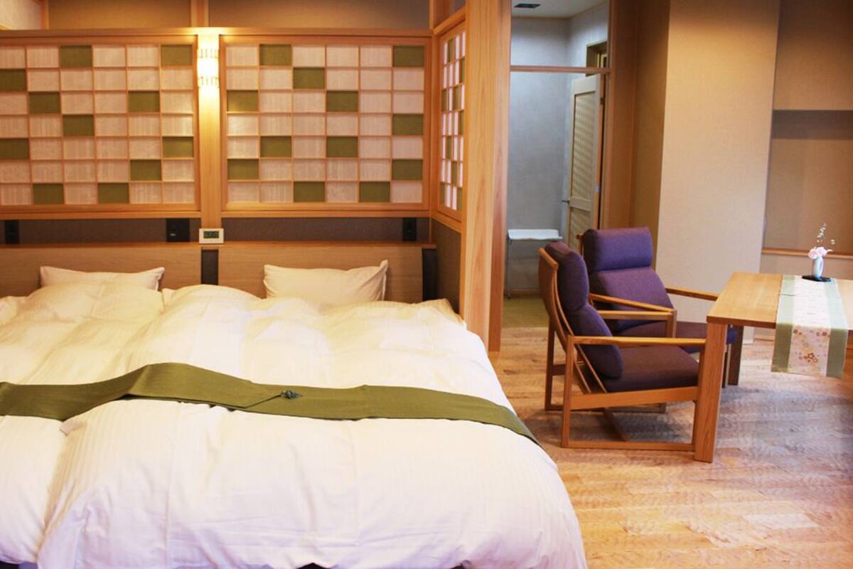 A hotel room with a large bed, a wooden headboard, a chair, and a small table.