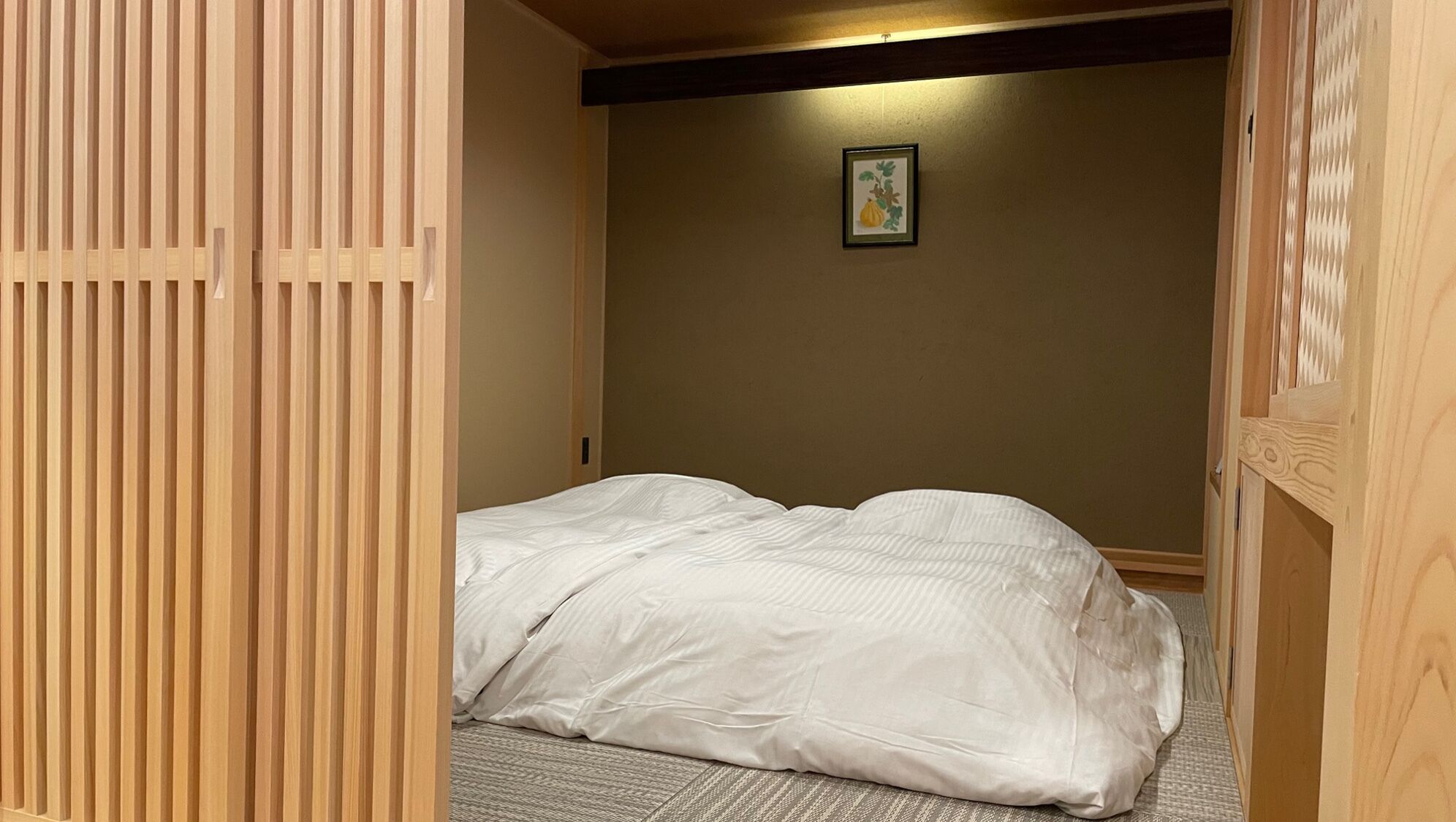Una habitación con una cama, un separador de listones de madera y un cuadro en la pared.