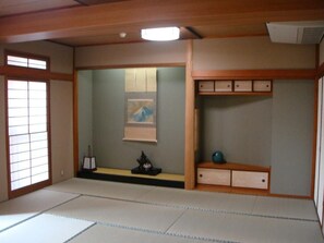 A traditional Japanese room with tatami flooring, a shoji screen, a painting, a small shrine, and a shelf with decorative items. - Yamaichi Bekkan (Hatsukaichi)