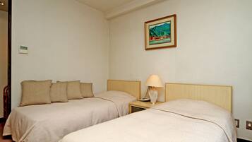 A hotel room with two single beds, a nightstand with a lamp, a painting on the wall, and a thermostat.