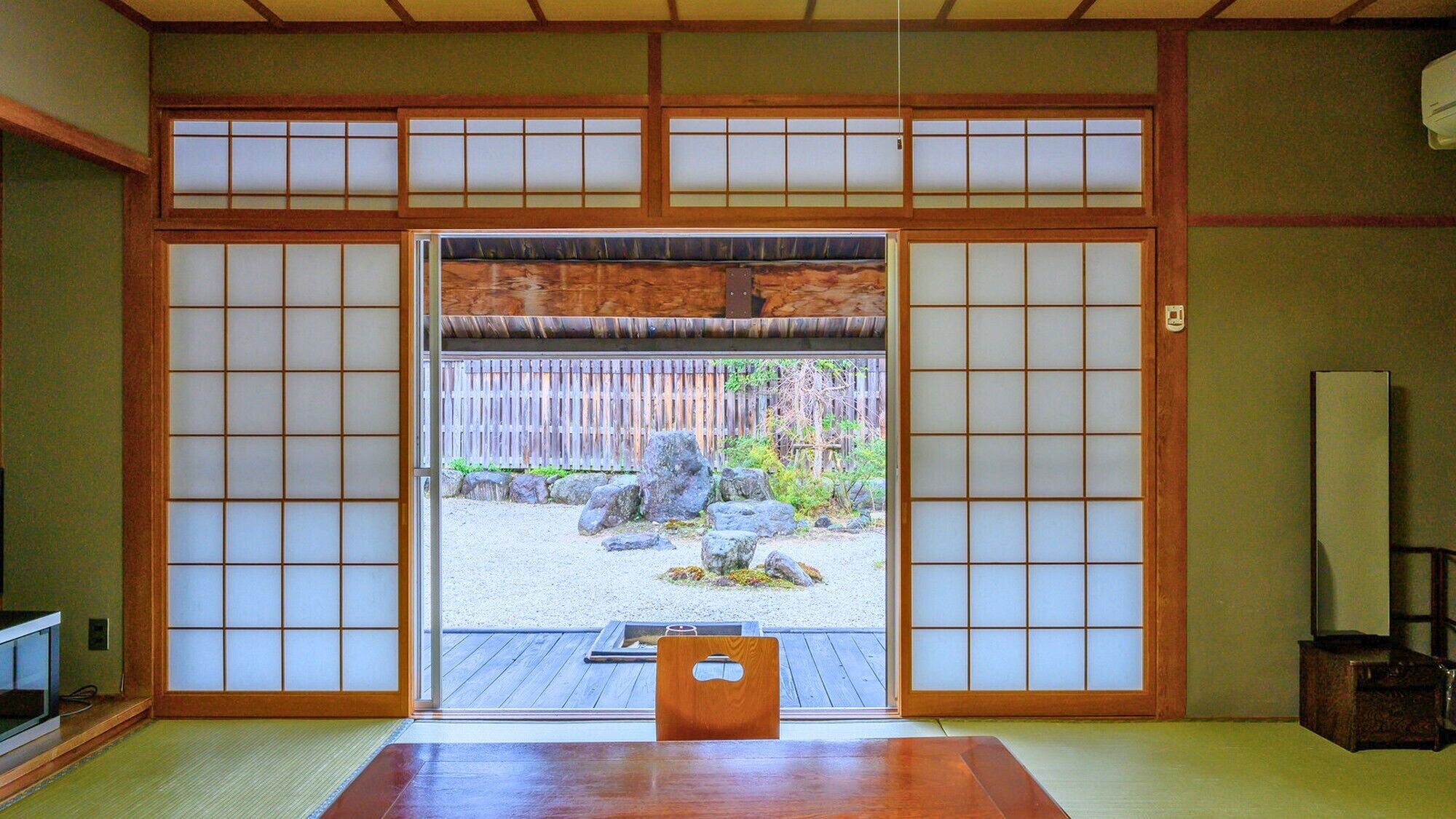 Una habitación japonesa tradicional con suelo de tatami, una puerta corredera que da a un jardín y una mesa de madera.