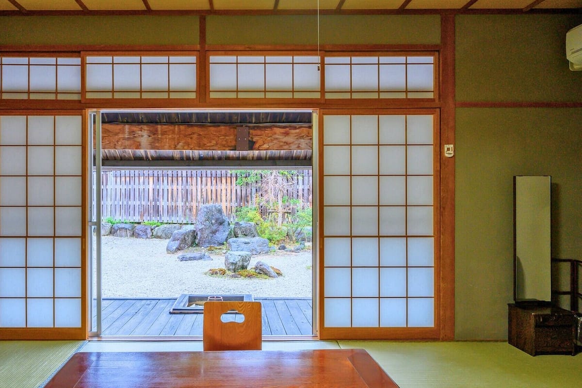 A traditional Japanese room with tatami flooring, a sliding door leading to a garden, and a wooden table.