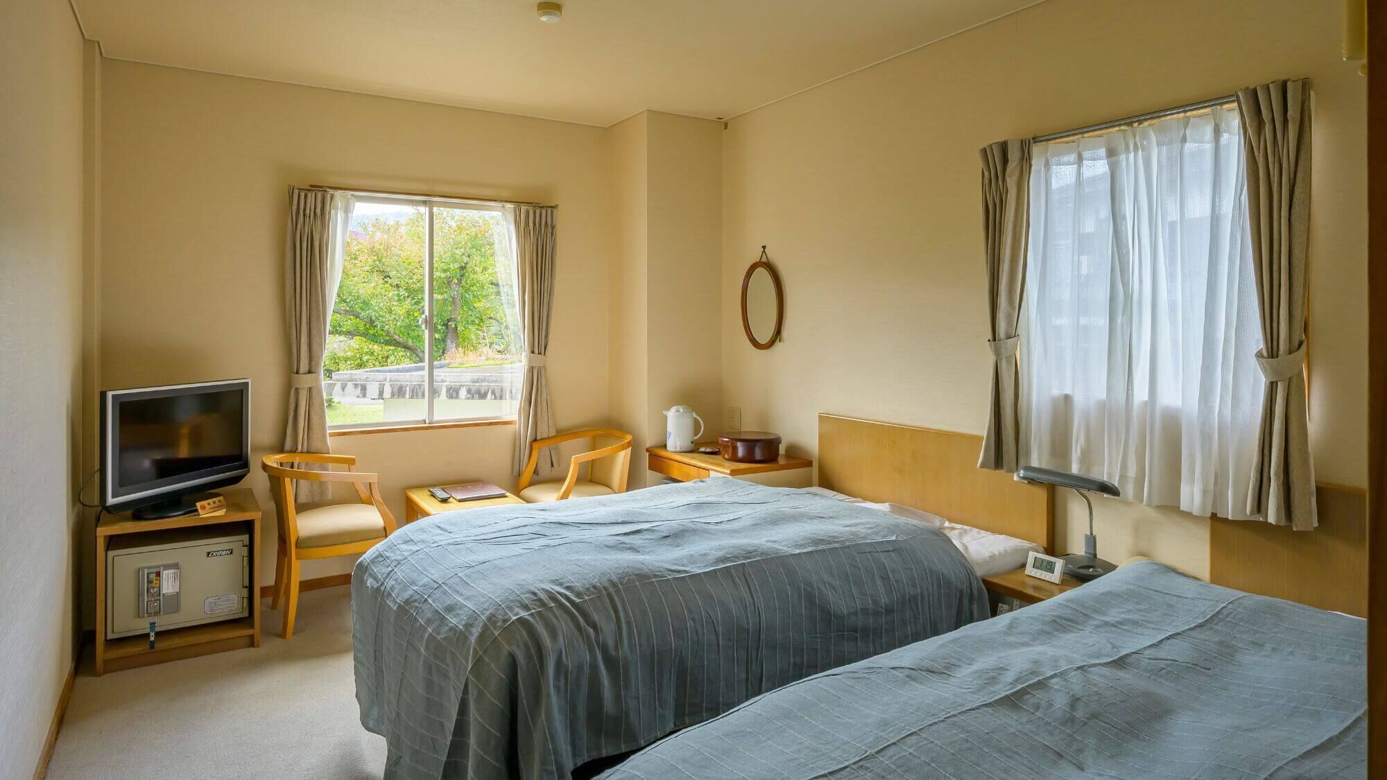 Habitación de hotel con dos camas, televisión, escritorio, silla y ventana con cortinas.