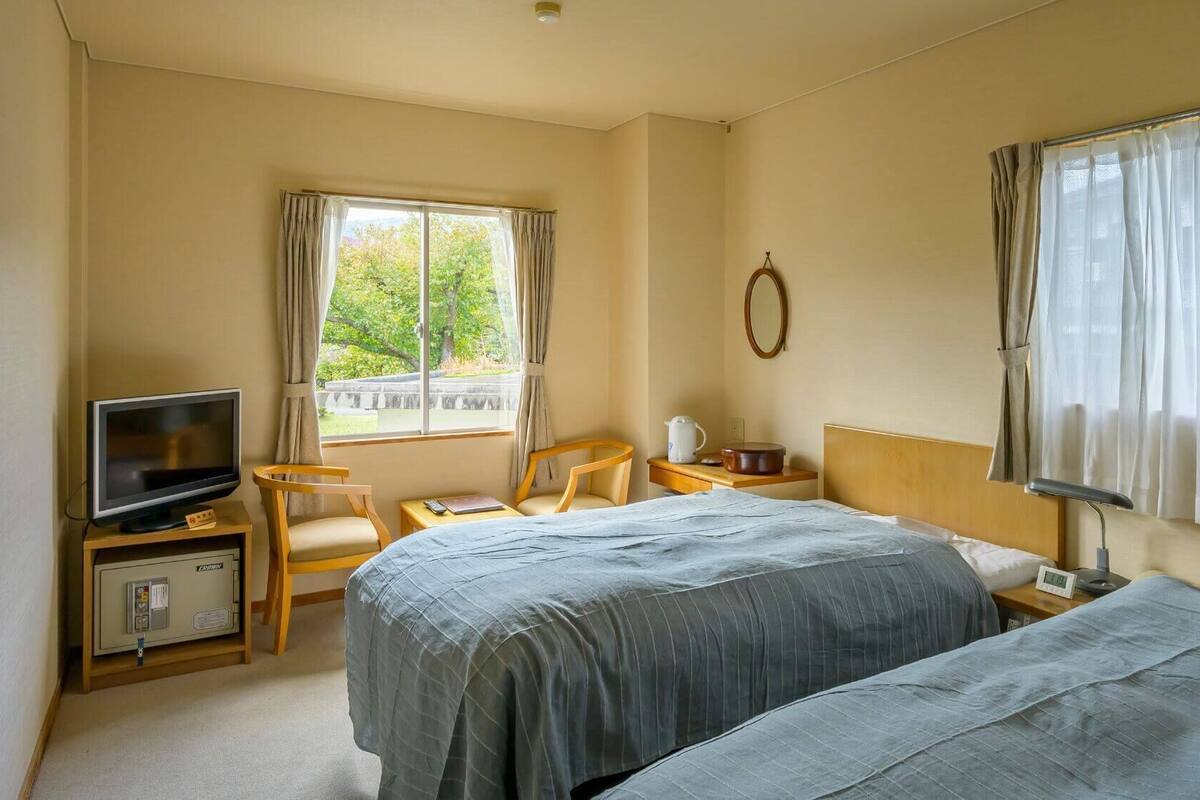 A hotel room with two beds, a TV, a desk, a chair, and a window with curtains.
