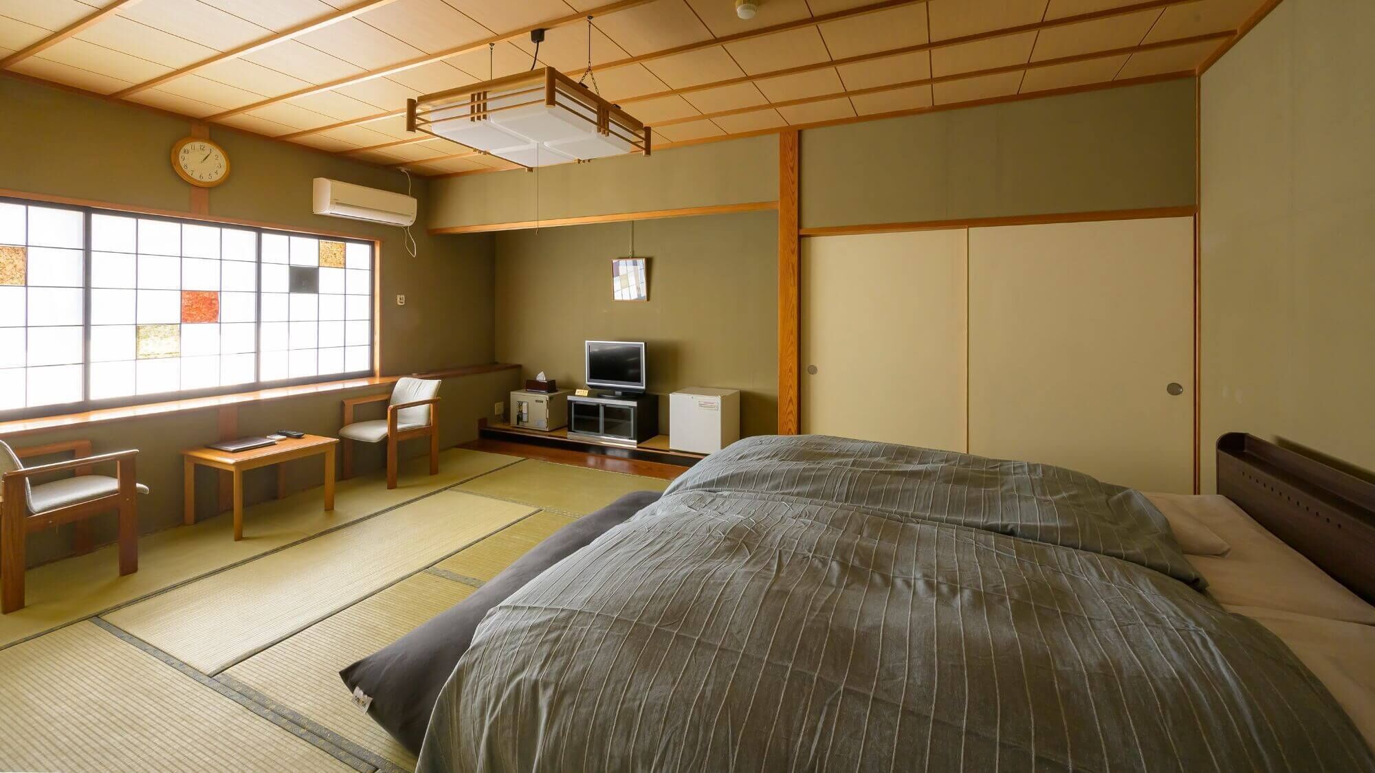 Una habitación japonesa tradicional con suelo de tatami, una cama, un escritorio con silla, un televisor y un armario.