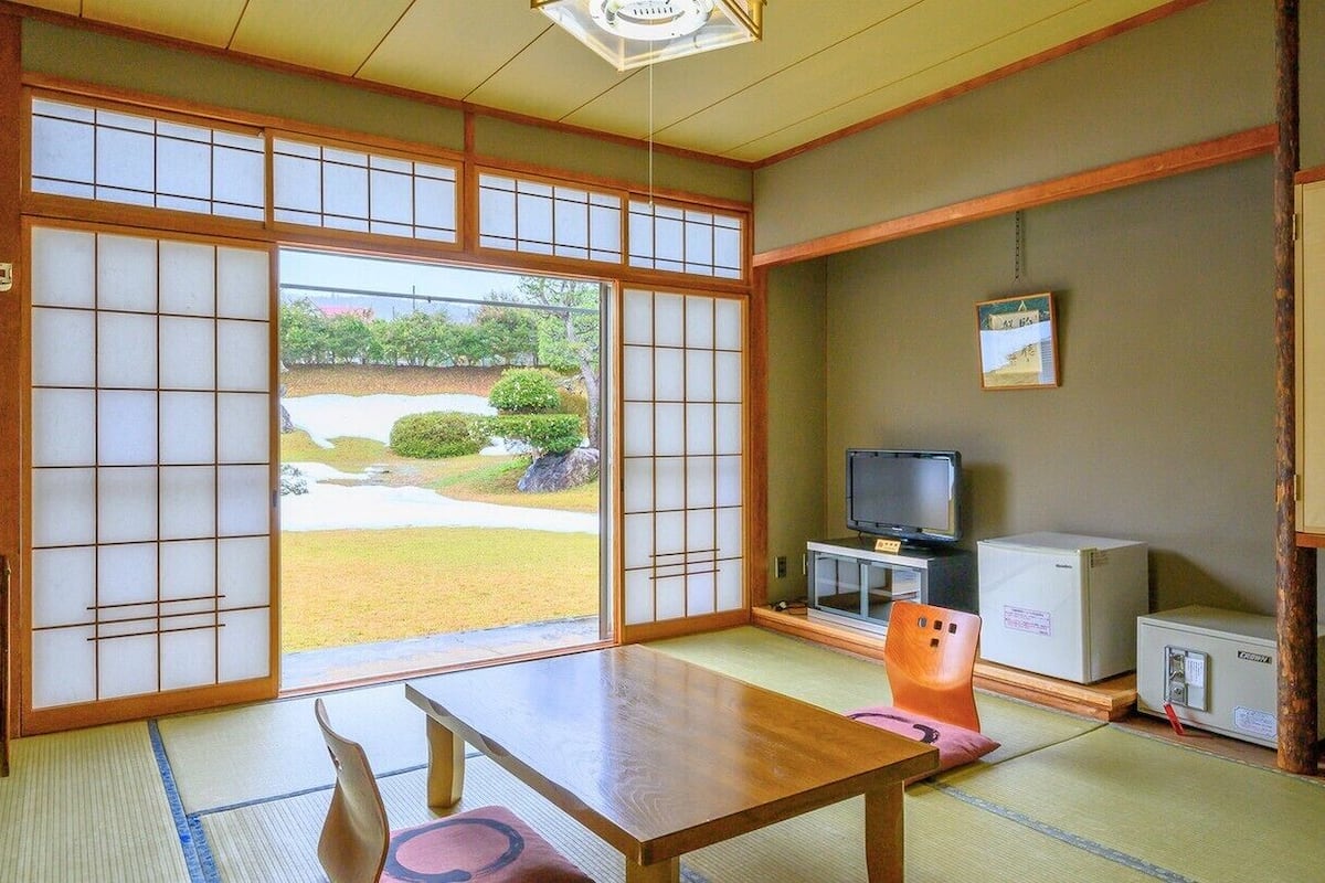 A traditional Japanese room with tatami flooring, a low table, a television, and a refrigerator.