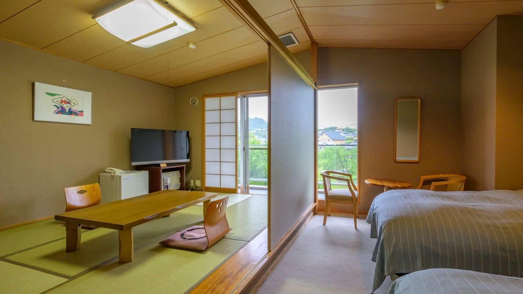 Una habitación japonesa tradicional con suelo de tatami, una mesa baja, un televisor y una puerta corredera que da a un balcón.