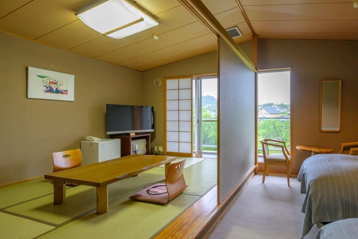 A traditional Japanese room with tatami flooring, a low table, a television, and a sliding door leading to a balcony.