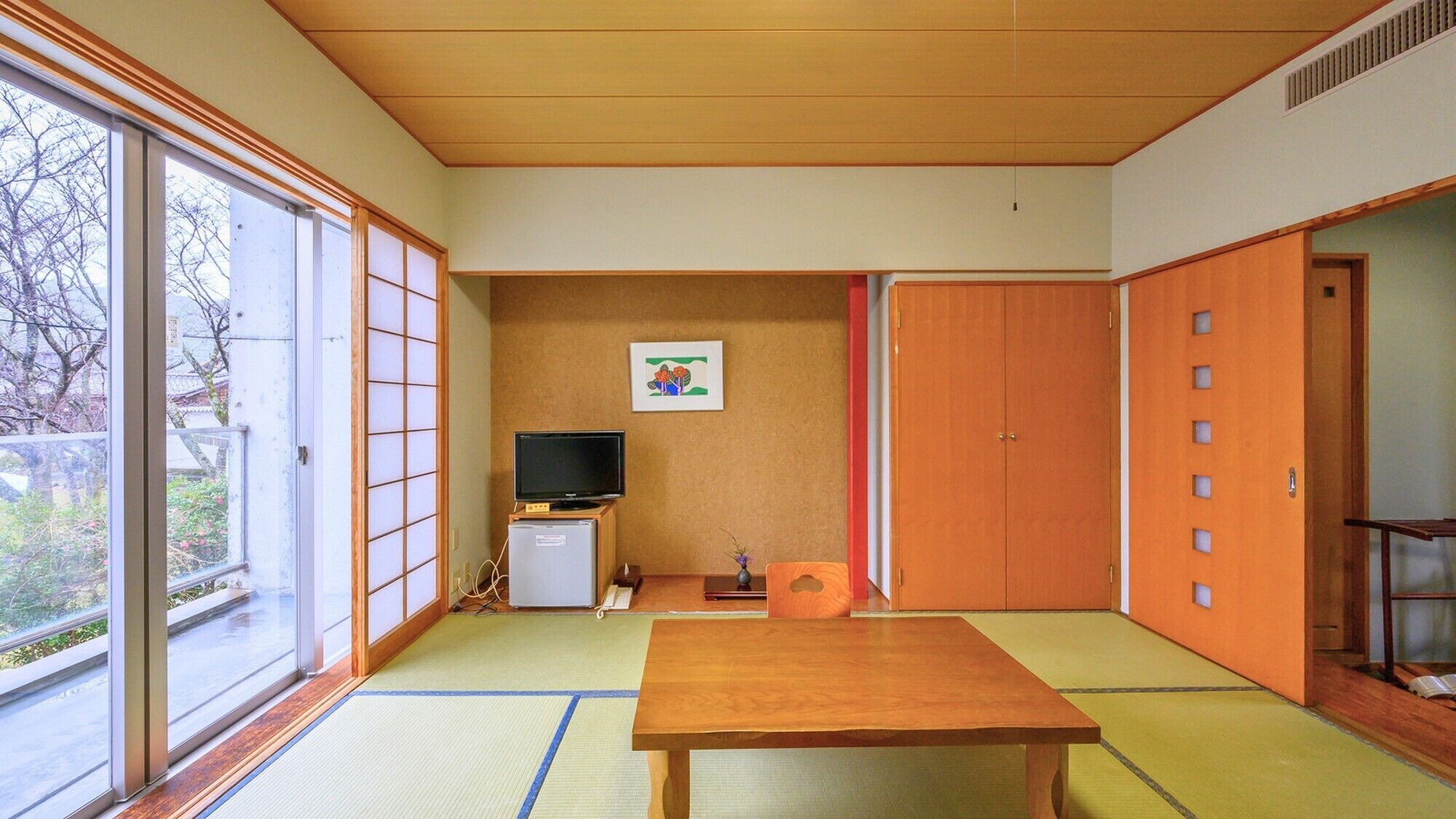 Una habitación tradicional japonesa con suelo de tatami, televisor, un mueble pequeño y puertas correderas.