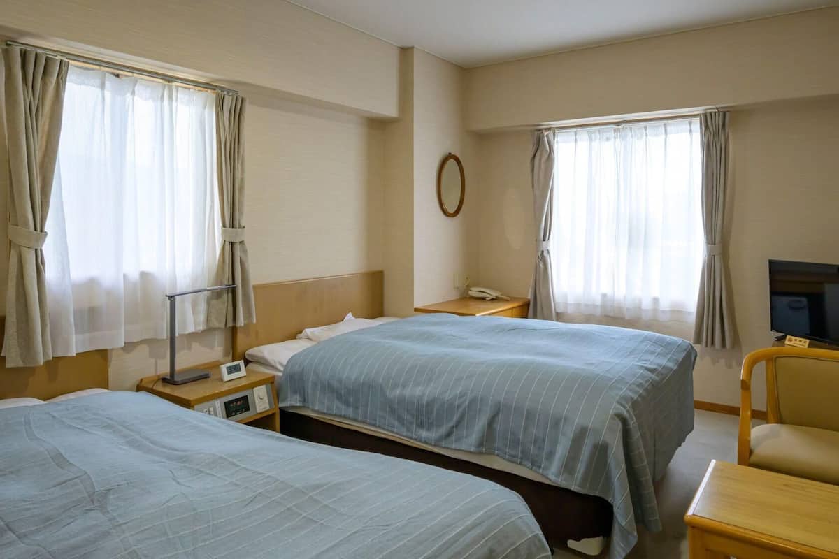 A hotel room with two beds, a TV, a desk, and a chair.