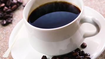 A white cup of black coffee on a white saucer with coffee beans scattered around.