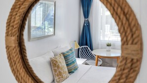 Espejo redondo con marco tejido que refleja una habitación con cama, almohadas, una mesita y una ventana con cortinas.