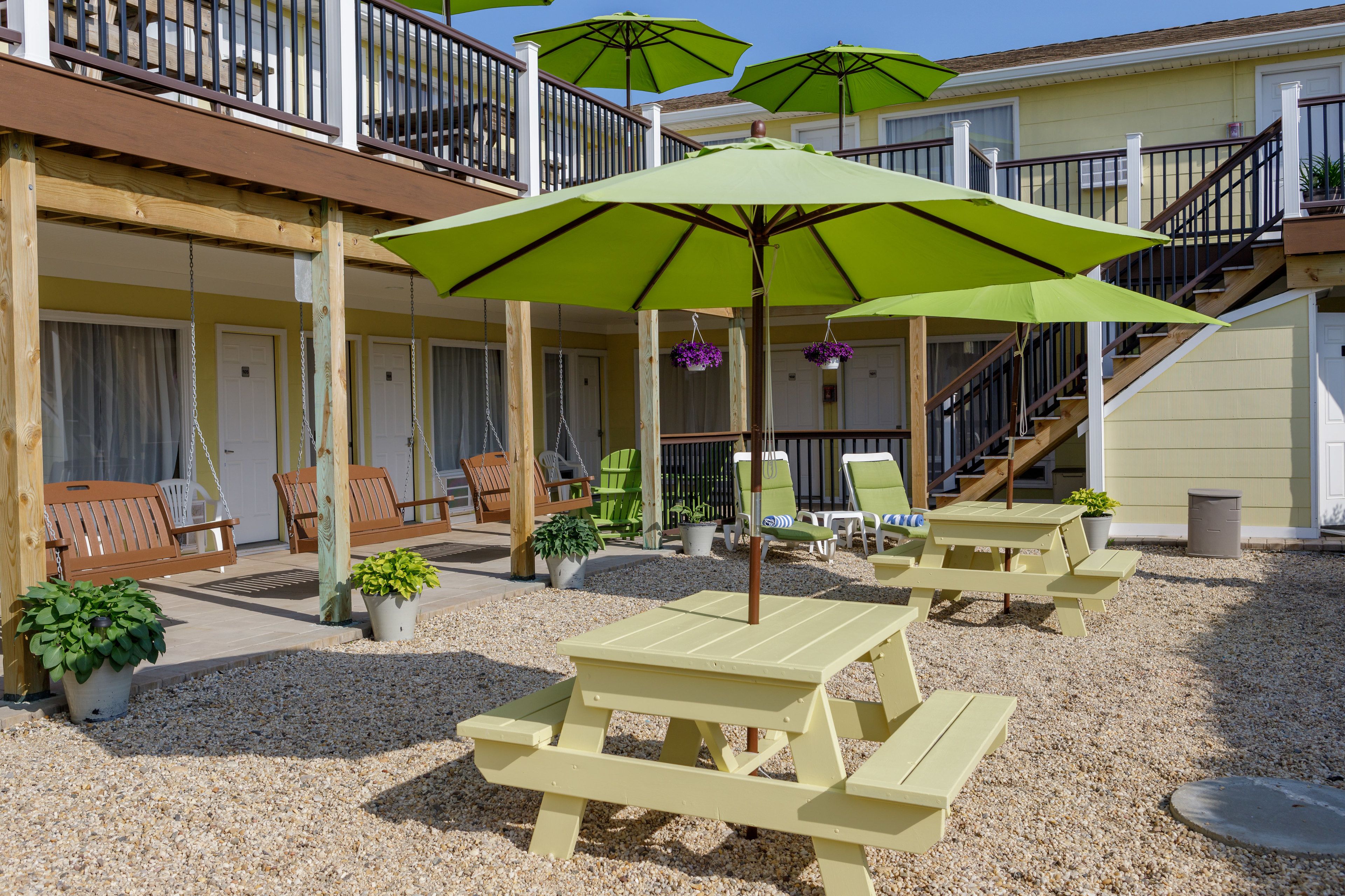 A patio area with outdoor seating, including picnic tables and chairs, and green umbrellas.