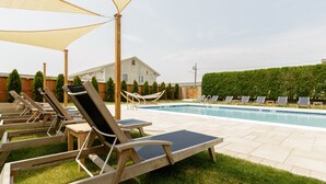 Un área junto a la piscina con tumbonas, un paraguas grande y una casa al fondo.
