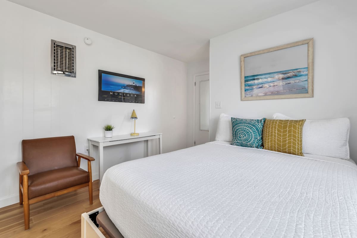 A bedroom with a large bed, a chair, a desk, and a wall-mounted TV.