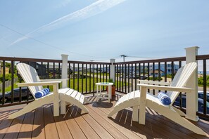 A wooden deck with two white Adirondack chairs and a small table, overlooking a parking area and buildings.
